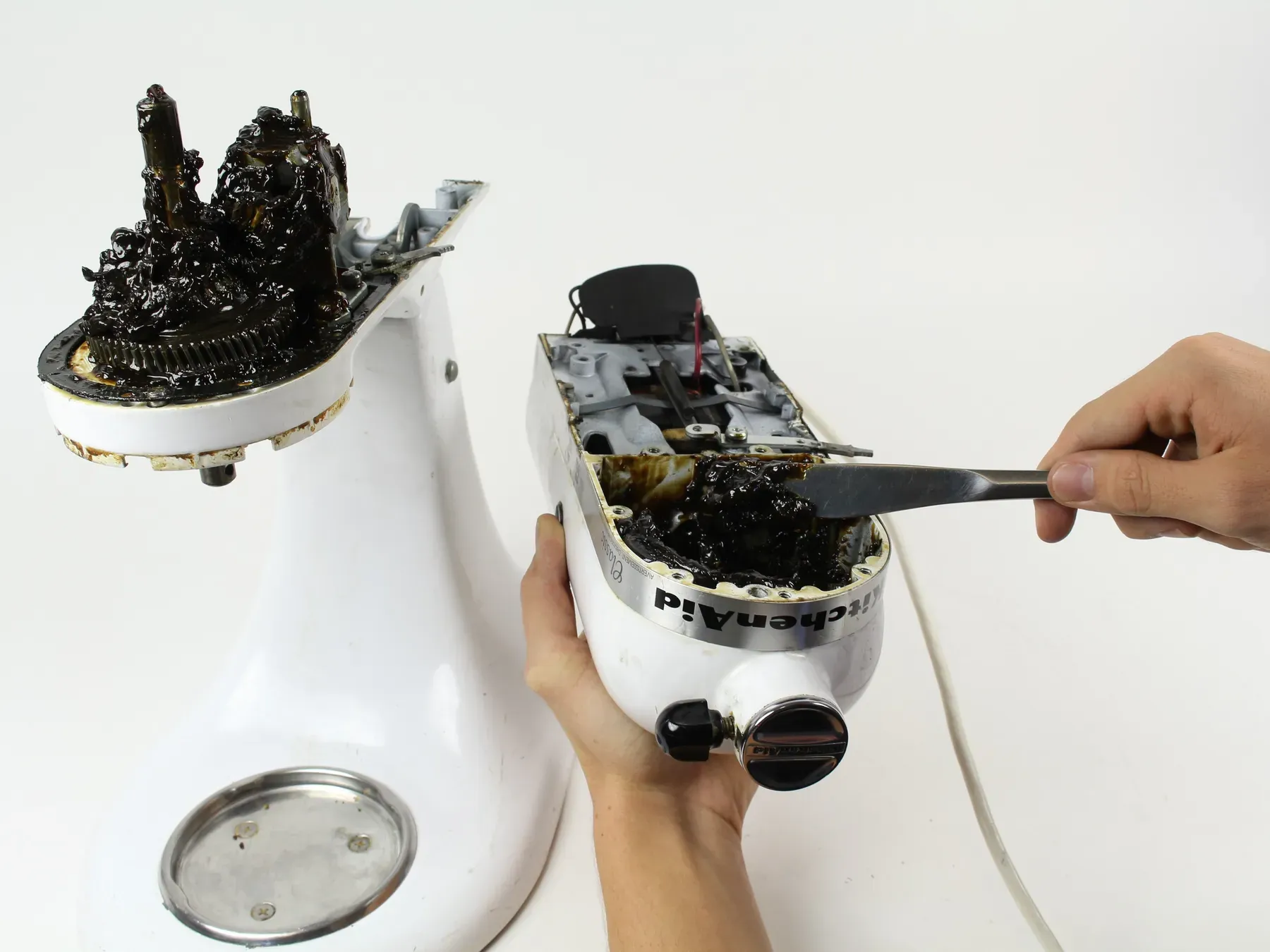 A KitchenAid mixer opened up on the bench, with old black grease being cleaned out of the gear housing